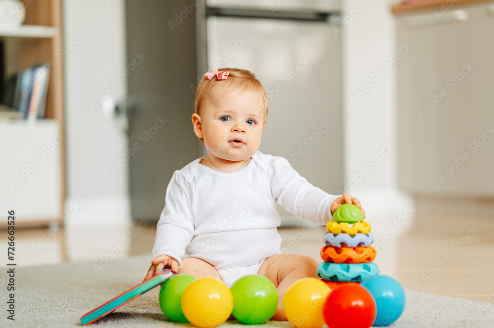 Cute baby girl is sitting on the floor at home while playing with her toys. Cute baby girl is sitting on the floor at home while playing with her toys.