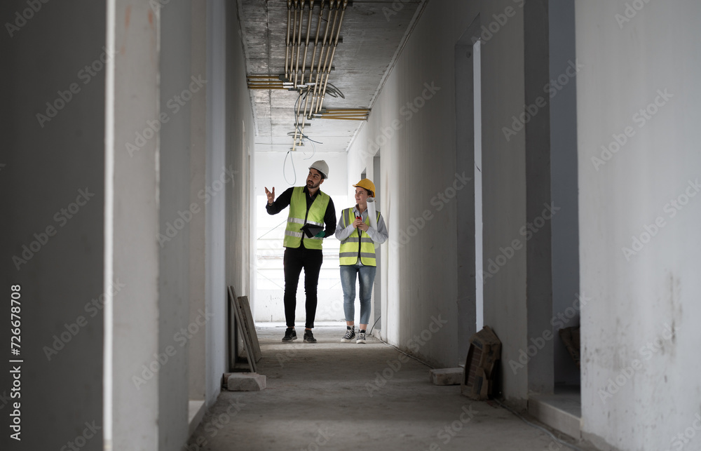 Caucasian engineer man and woman working with tablet computer and paper work in building at construction site	