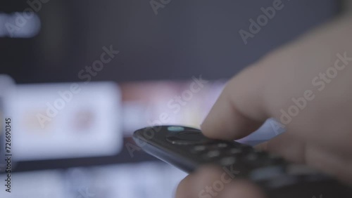 Man watches smart TV and uses black remote control. Person controls TV using a modern remote control choosing channels from a smart tv. Closeup 4k cinematic shot. Shallow depth of field