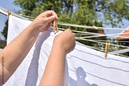 A woman hangs white sheets and tablecloths to dry after washing outdoors and attaches them with a clothespin.