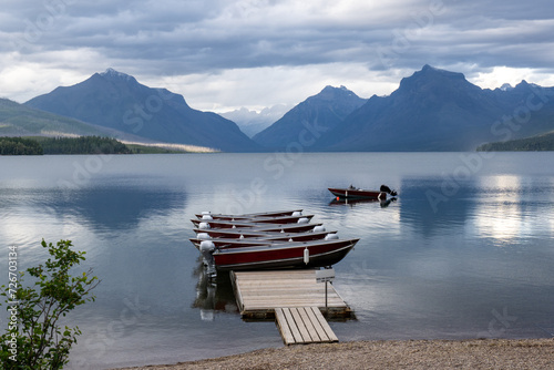 Nine small motor boats stacked on a dock while a 10th boat in the lakes water, Apgar Village, Lake McDonald, Glacier National Park, Montana photo