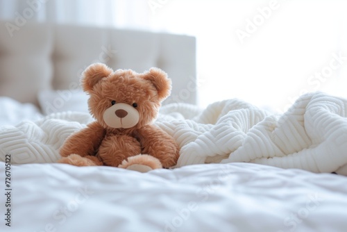 Cute little teddy bear lying alone on white bed in morning