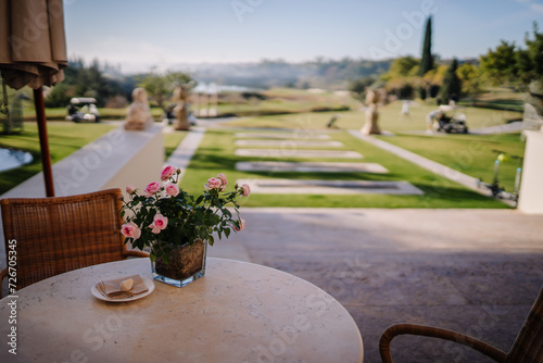 Sotogrante, Spain - January 26, 2024 -  table with a vase of pink roses overlooking a landscaped garden and golf course. photo
