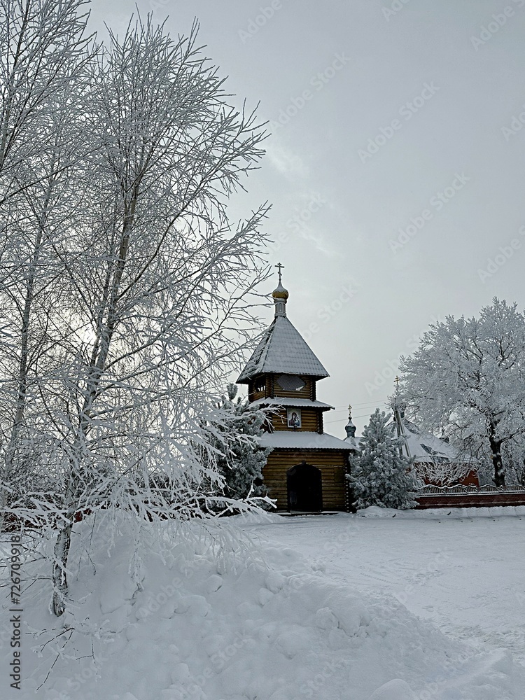 wooden bell tower against a background of snow-covered trees. Kazan Alexievo-Sergievskaya hermitage. Penza region Russia