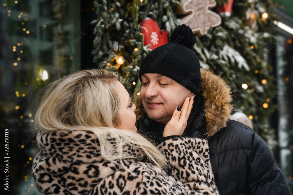 Love romantic couple lovestory. Man hugging woman, kissing girl in Christmas winter fur trees decoration. Romantic date. Walking,having fun. Stylish clothes,fur leopard print coat, black jacket, hat