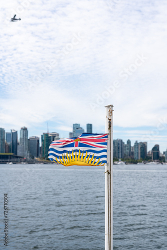 A British Columbia Flag flapping in the wind with the Vancouver Skyline and a Seaplane in the background.