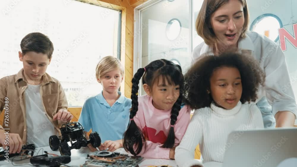 Teacher teach and explain students about digital electrical tool or car model. Diverse kid learn electronic equipment and use to fix motherboard or robotic model at table with wires placed. Erudition.