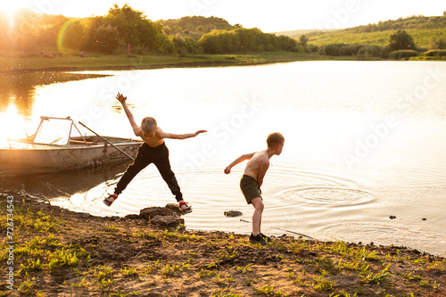 Two little boys is having fun jumpings from the boat on the shore of the lake, their's jumps with his arms and legs outstretched. Horizont view.