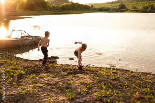 Back view of a two brothers kids play near lake throw stones together.