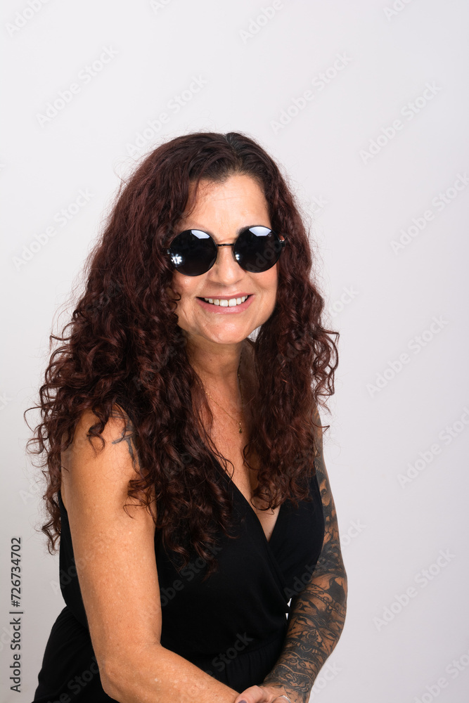 Beautiful curly-haired woman wearing sunglasses and black clothing smiling.
