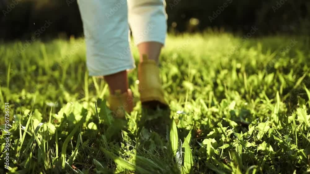 Gardener female person feet in yellow rubber boots walks on green grass and rubble land road ground. Autumn season. Close-up. Gardener female person feet in yellow rubber boots walks on green grass and rubble land road ground. Autumn season. Close-up.