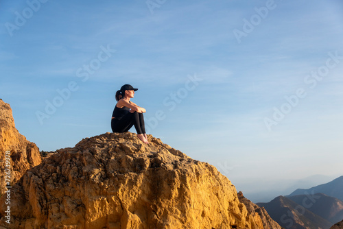 Sporty woman sitting on top of a rock looking at the view of mountains, summer vacation.