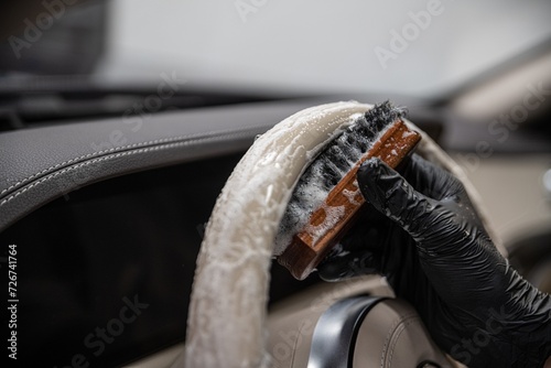 Car wash employee or a car detailing studio thoroughly cleans a light leather steering wheel with a brush and detergent