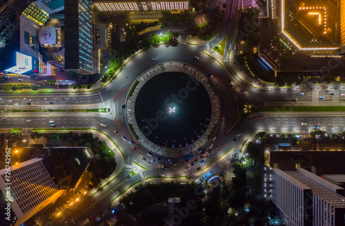 Top down overhead aerial view of moving car traffic at roundabout Vehicle road traffic around Selamat Datang monument in Jakarta, Indonesia at night