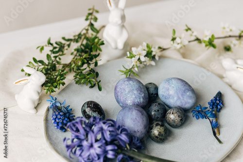 Stylish easter eggs on vintage plate, bunny and spring flowers on rustic table. Happy Easter! Natural dye blue eggs, purple hiacynt blossoms on linen napkin. Holiday setting, minimal still life