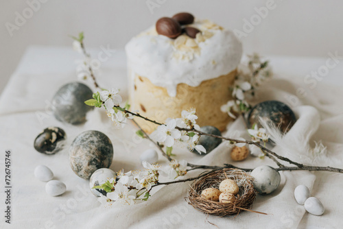 Stylish easter eggs, panettone, spring flowers and chocolate eggs on linen cloth on rustic table. Natural dye marble eggs and cherry blossom, minimal still life. Happy Easter!
