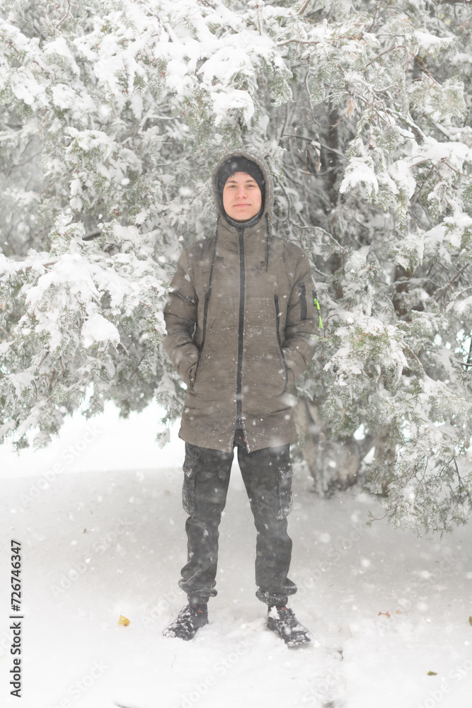 a boy is posing with snow on the street, it is snowing, a blizzard and frost on a winter day