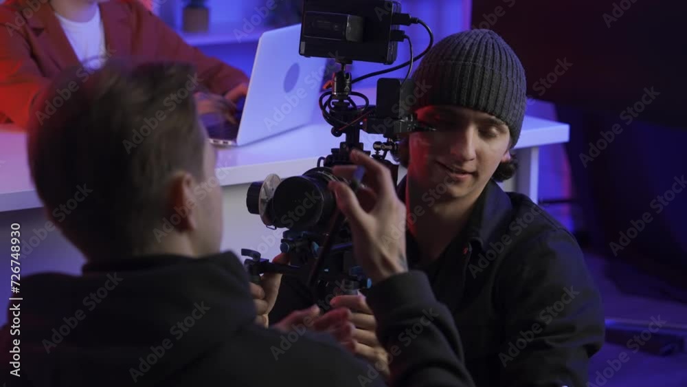 A cameraman filming a TV presenter gives a smartphone with the camera turned on to an assistant. A man wants his assistant to take photos and videos of him while working. A cameraman filming a TV presenter gives a smartphone with the camera turned on to an assistant. A man wants his assistant to take photos and videos of him while working.