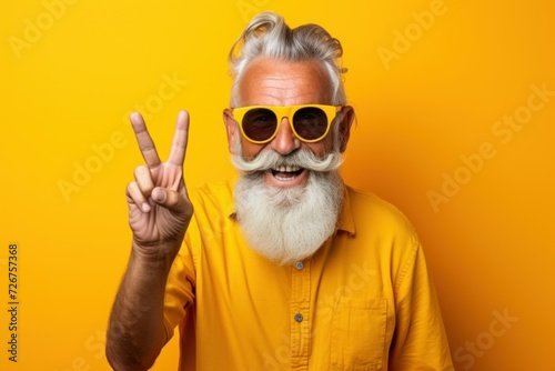 handsome elderly man showing two fingers up as a victory gesture on a bright yellow background, studio photo, basis for advertising, banner