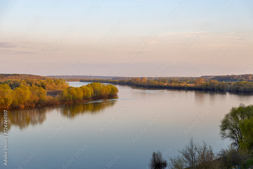A wide river on a spring evening as seen from a hill.