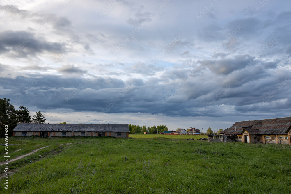 Fototapeta premium Rural landscape with an old cowshed in the background of a landscape with clouds. abandoned mission
