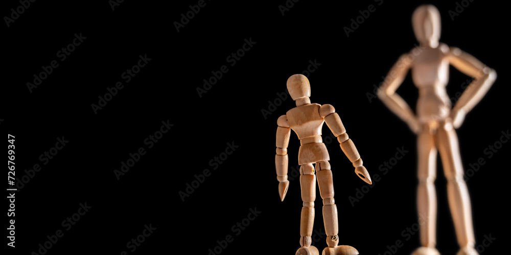 Kleine und große Holzfigur vor schwarzem Hintergrund zum Thema Autorität und Selbstwertgefühl Kleine und große Holzfigur vor schwarzem Hintergrund zum Thema Autorität und Selbstwertgefühl