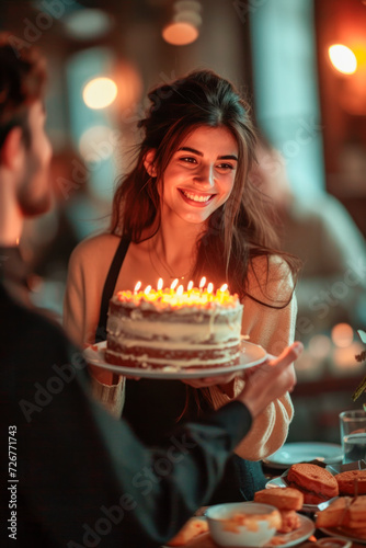 Portrait of a young Hispanic woman smiling while celebrating her birthday in a restaurant, a young guy serving her a cake with candles. Vertical