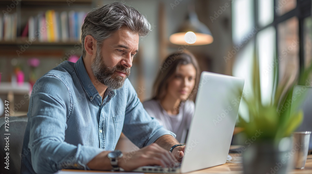Fototapeta premium A Man Sitting at a Table Using a Laptop Computer