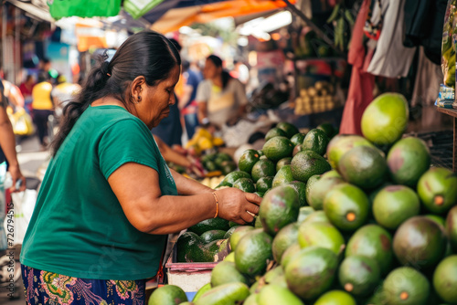 woman buying avocados from a street vendor in a busy market. The vendor is wearing a green shirt, and there are other vendors selling goods nearby photo