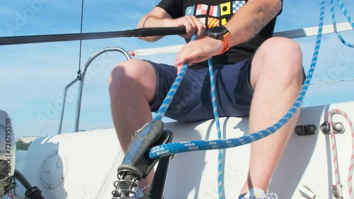Man with force pulls rope sitting on sailboat deck. Experienced traveler controls position of mainsail pulling ropes going downwind photo