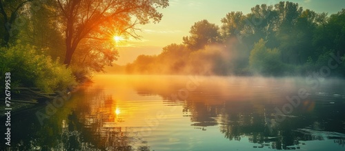 The river reflects the sun, trees, and mists of a morning.