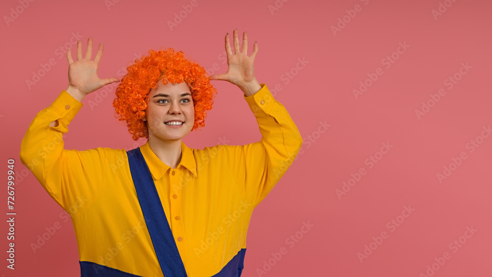 cheerful smiling clown in a wig and a yellow-blue suit raised up his hands and shows empty palms on a colored background with copy space cheerful smiling clown in a wig and a yellow-blue suit raised up his hands and shows empty palms on a colored background with copy space