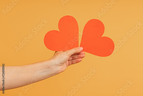 A hand holding two red paper hearts slightly apart
