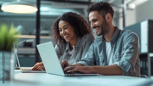 Cheerful businesspeople using a laptop in an office. Happy young entrepreneurs smiling while working together in a modern workspace. Two young businesspeople sitting together at a tabl : Generative AI