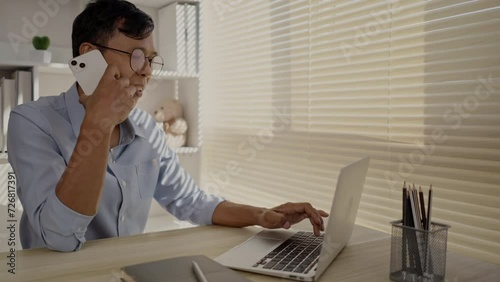 Man Multitasking, Typing on Laptop and Talking on Phone at Home Office , Home Workspace, Very busy with work.