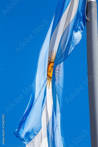 Argentine flag flying on a flagpole against a blue sky on a sunny day. Patriotic symbol of Argentina.