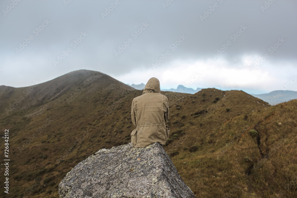 lonely, unrecognizable guy sitting on a rock in the middle of the Paramo in a foggy environment