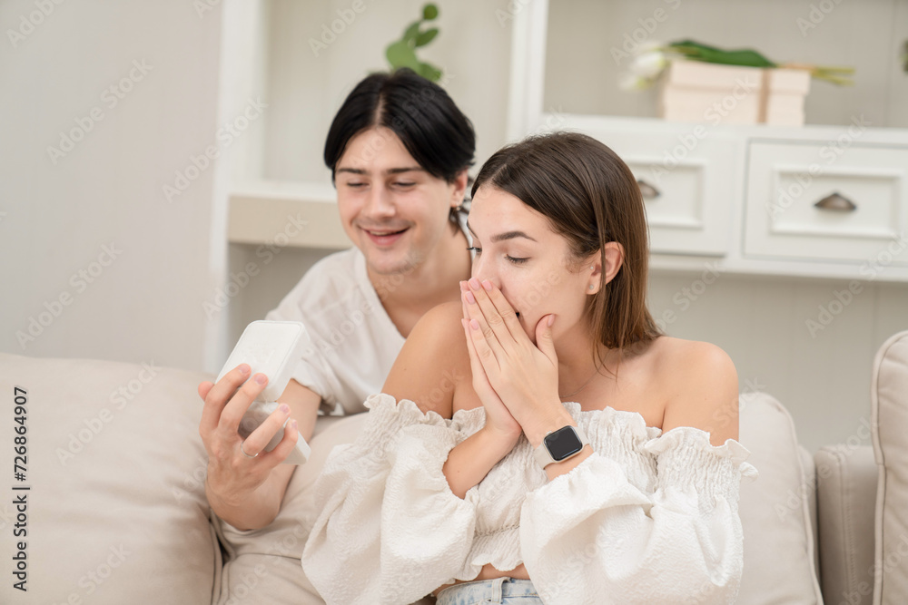 A young man putting the necklace around his girlfriend's neck in the kitchen on Valentine's Day Valentine's Day concept. Lovers at home celebrating Valentine's Day