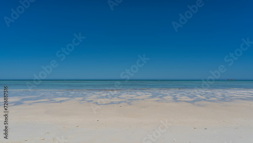 A paradisiacal minimalistic seascape. Sandy beach, aquamarine ocean, clear blue sky. Puddles and rivulets of water on the white sand. Madagascar. Nosy Iranja 