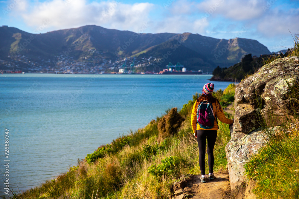 Fototapeta premium hiker girl admiring the idyllic scenery of lyttelton bay at coastal cliff walk from hays bay to church bay and diamond bay, banks peninsula, canterbury, new zealand