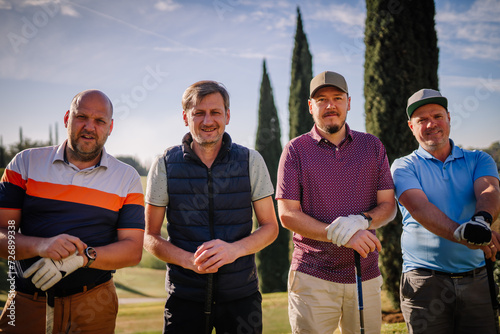 Sotogrante, Spain - January 26, 2024 - four men standing on a golf course, wearing casual golf attire and gloves, holding golf clubs, with trees in the background.