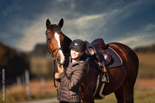 Horse stands with his rider on a meadow in the sun ready to ride out.