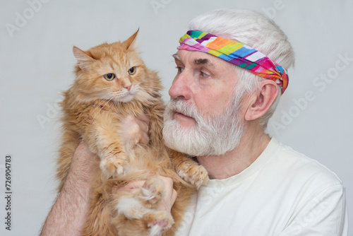 an elderly handsome man with a gray beard holds a Big red Siberian cat in his hands photo