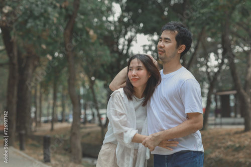 Happy young Asian couple in a park, Portrait of smiling couple near beautiful nature outdoors, lifestyle, Cheerful couple hugging each other, Young couple enjoying the sunny day at park