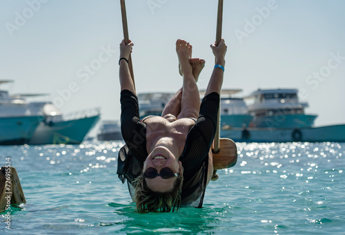Joyful girl swings upside down on a swing in the sea photo