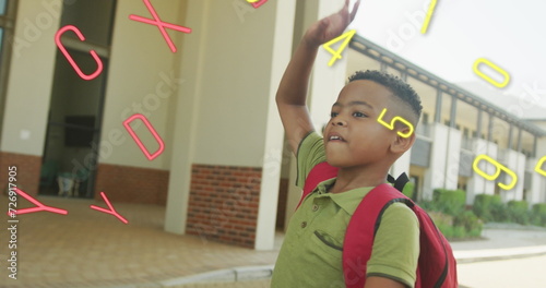 Image of numbers and letters over happy biracial schoolboy waving outside school