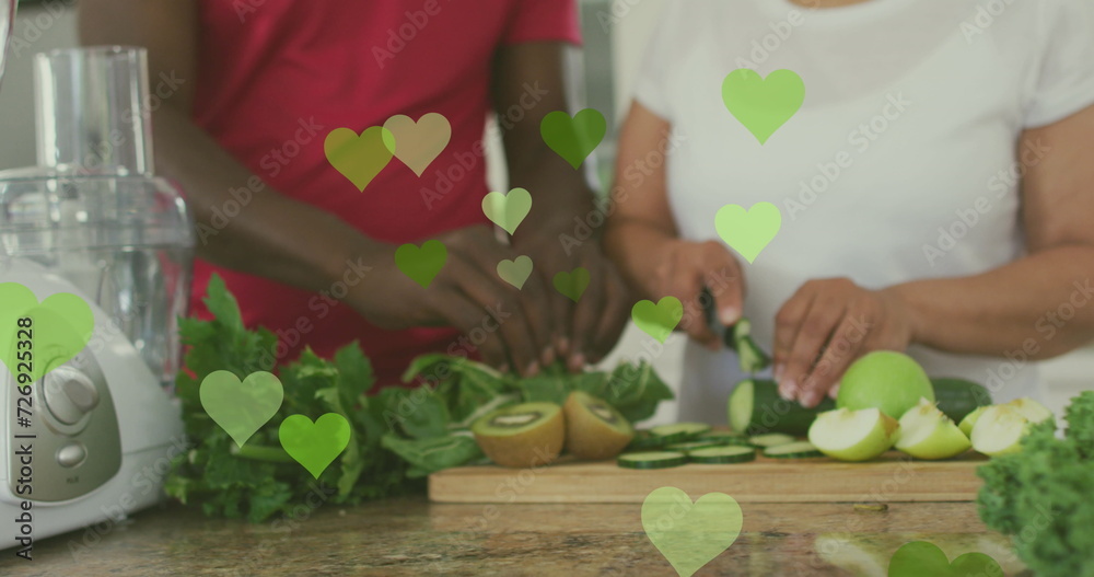 Image of hearts over senior african american couple cooking