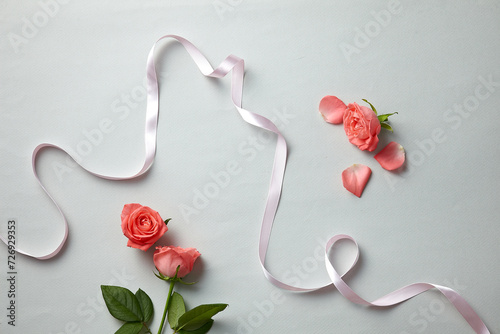 a beautiful pink rose and ribbon against a light grey blue paper background. top view. An empty space for display cosmetic products, food and props.