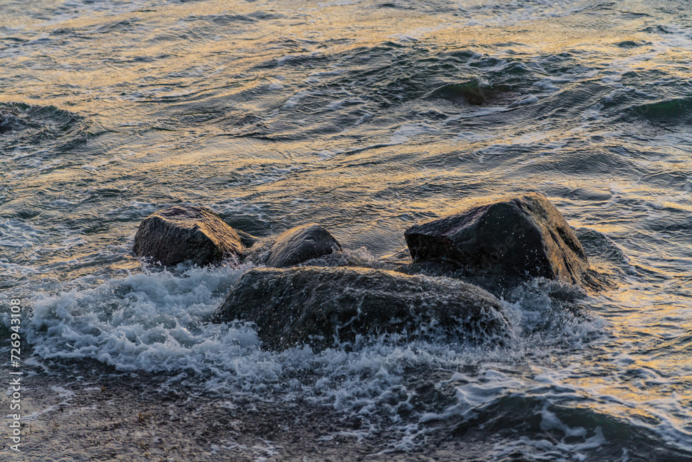 Fototapeta premium Waves crashing over big rocks from view above in cold ocean