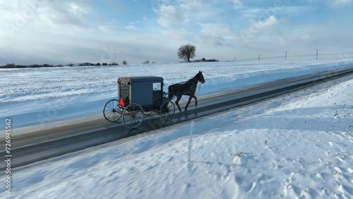 Horse and buggy in Amish Country. Snow covered road after blizzard. Aerial tracking shot. photo